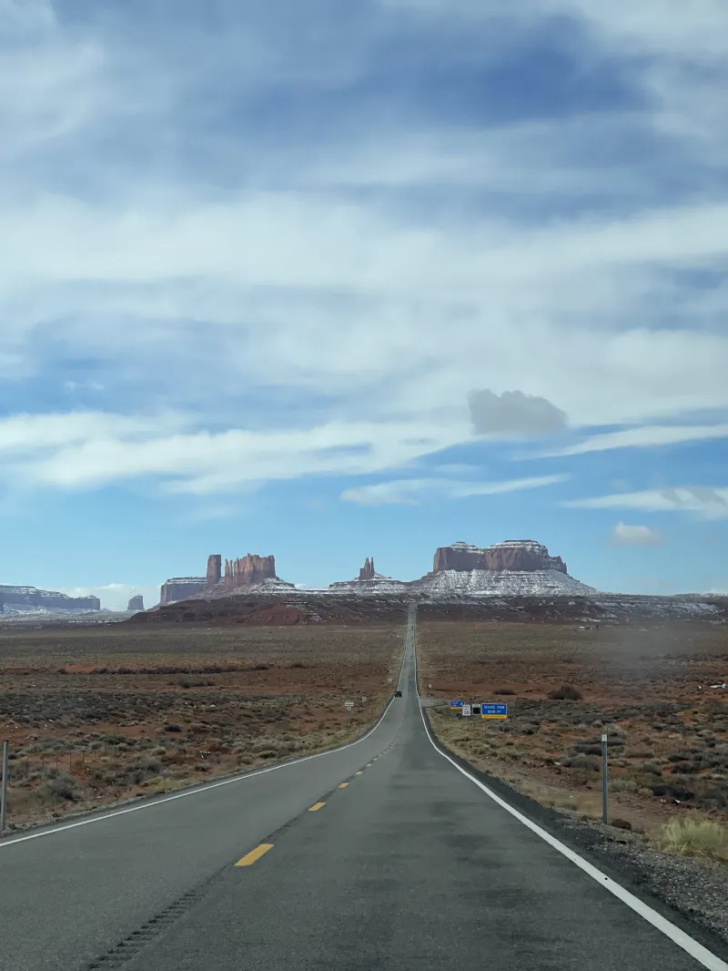 Long road leading to Monument Valley with cloudy sky and desert landscape.