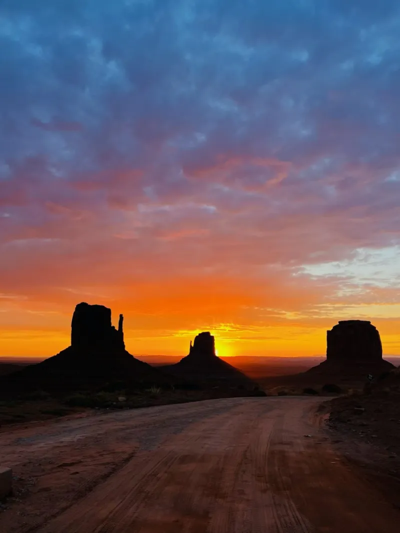Sunset over Monument Valley with silhouetted rock formations and colorful sky.